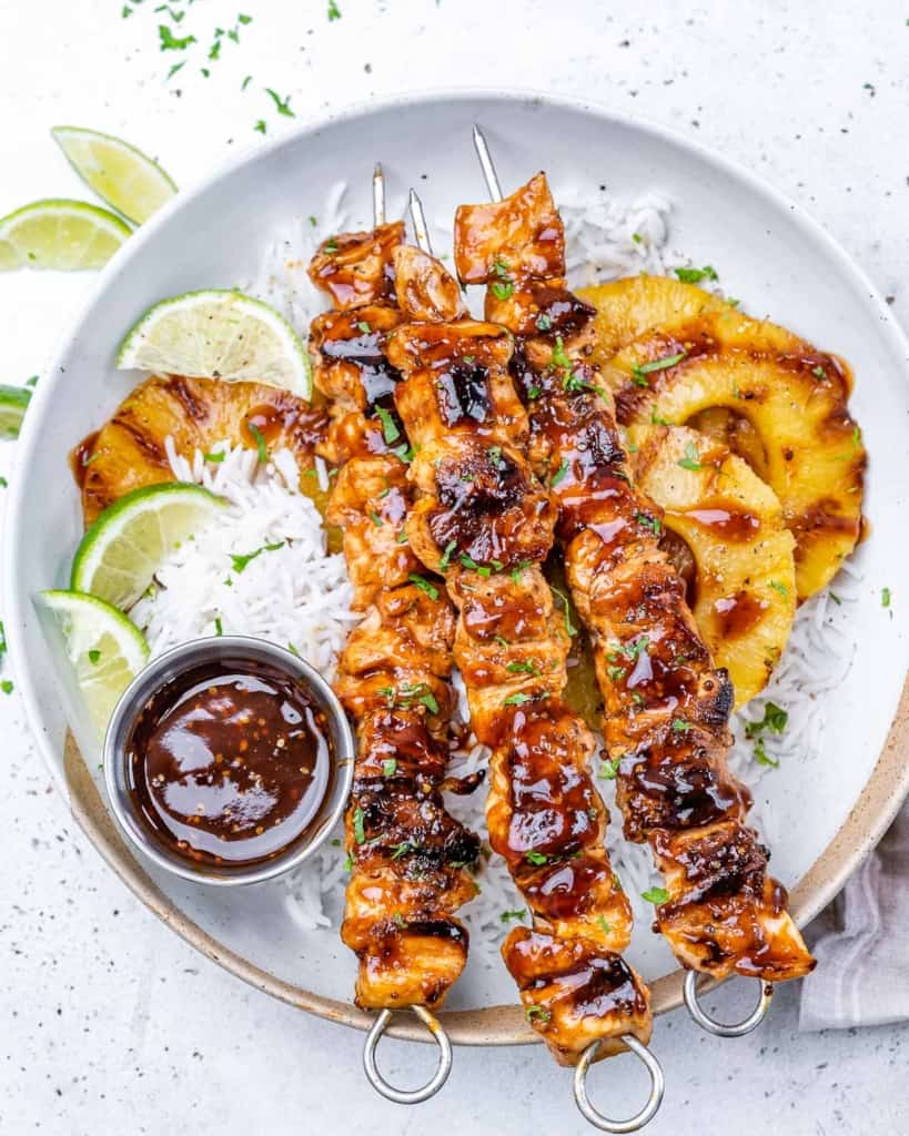 One plate with huli huli chicken on skewers with rice and pineapples