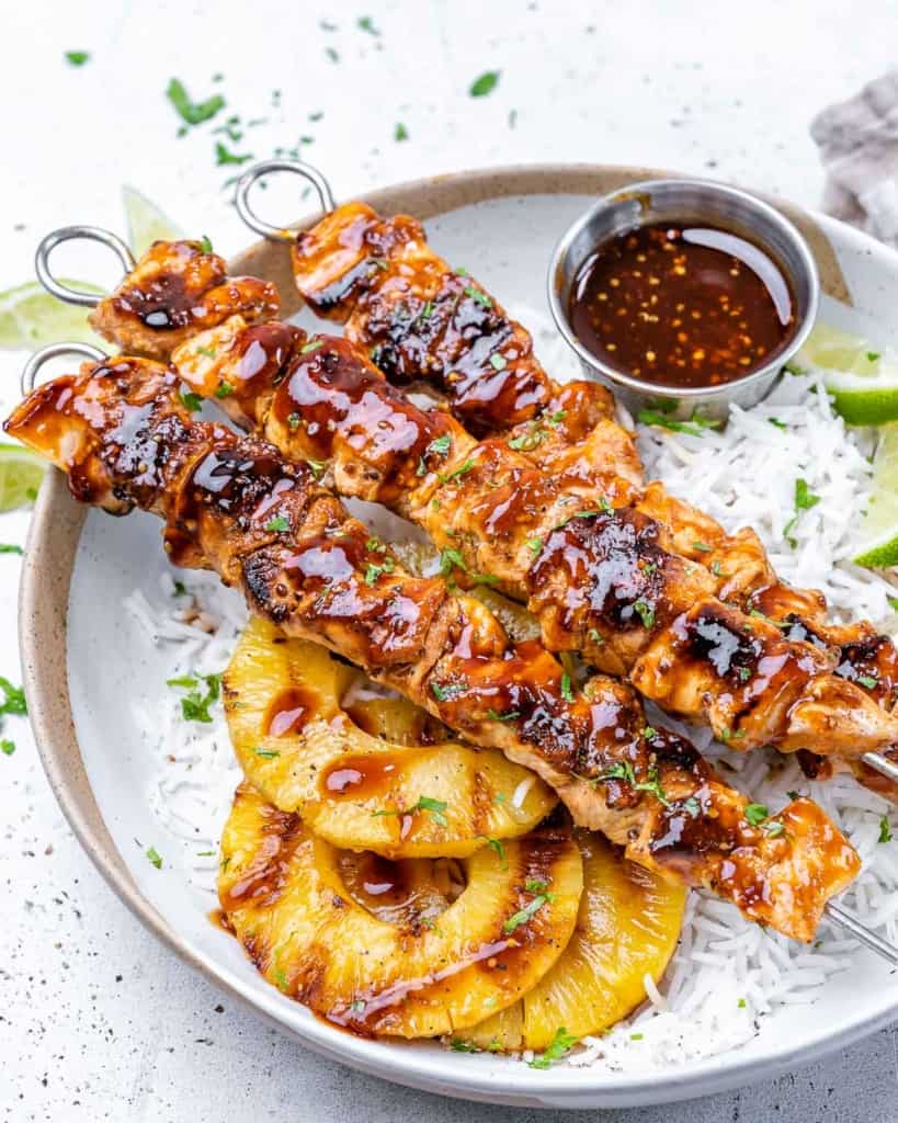 Chicken on skewers over bed of rice on plate with pineapple