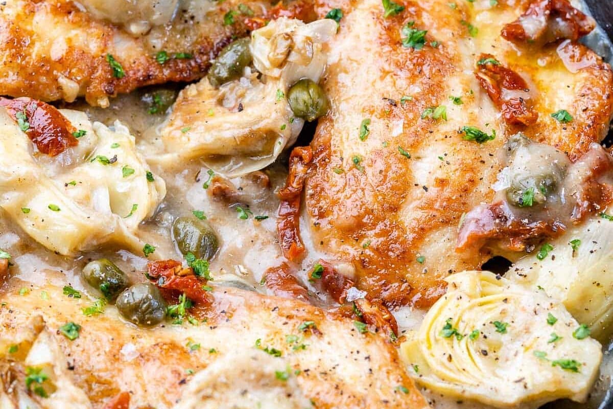 close up view of seared chicken in a black skillet with capers lemon sauce