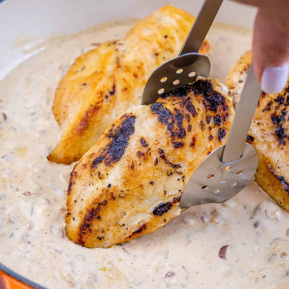 chicken being put in skillet with tongs 