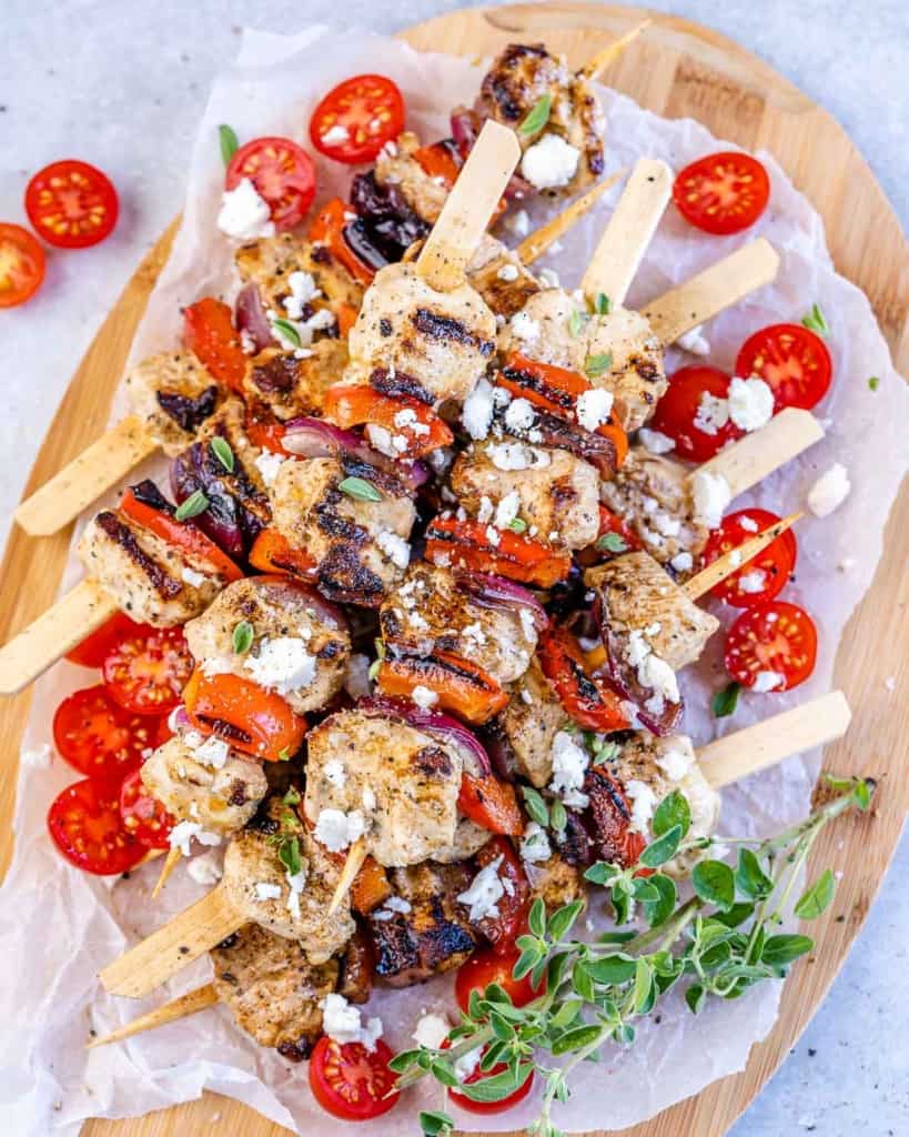 top view chicken skewers with tomato garnishes and feta cheese on a brown cutting board