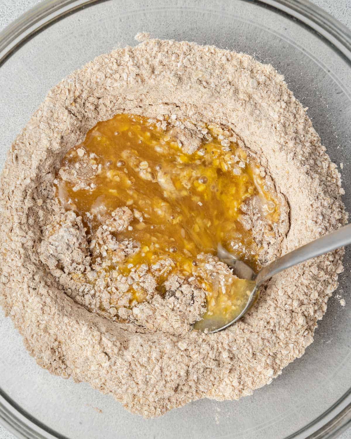 spoon mixing the egg and wet mixture with the flour mixture in a bowl.