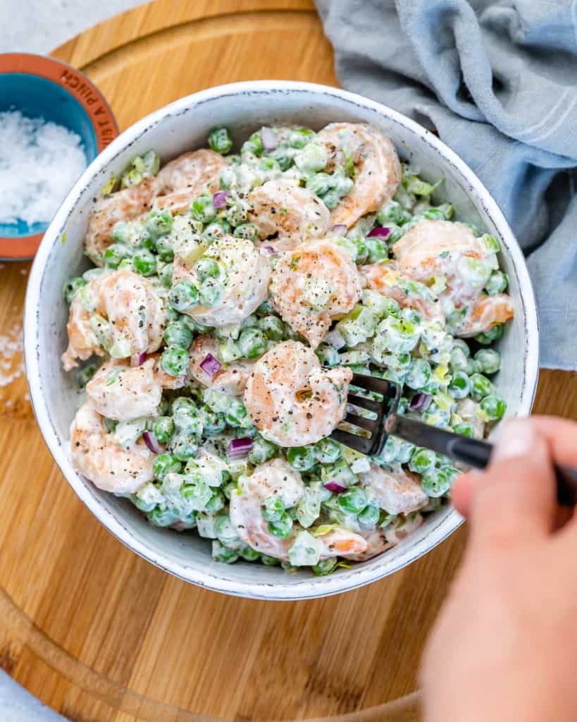 hand holding black fork being dipped into the shrimp salad bowl