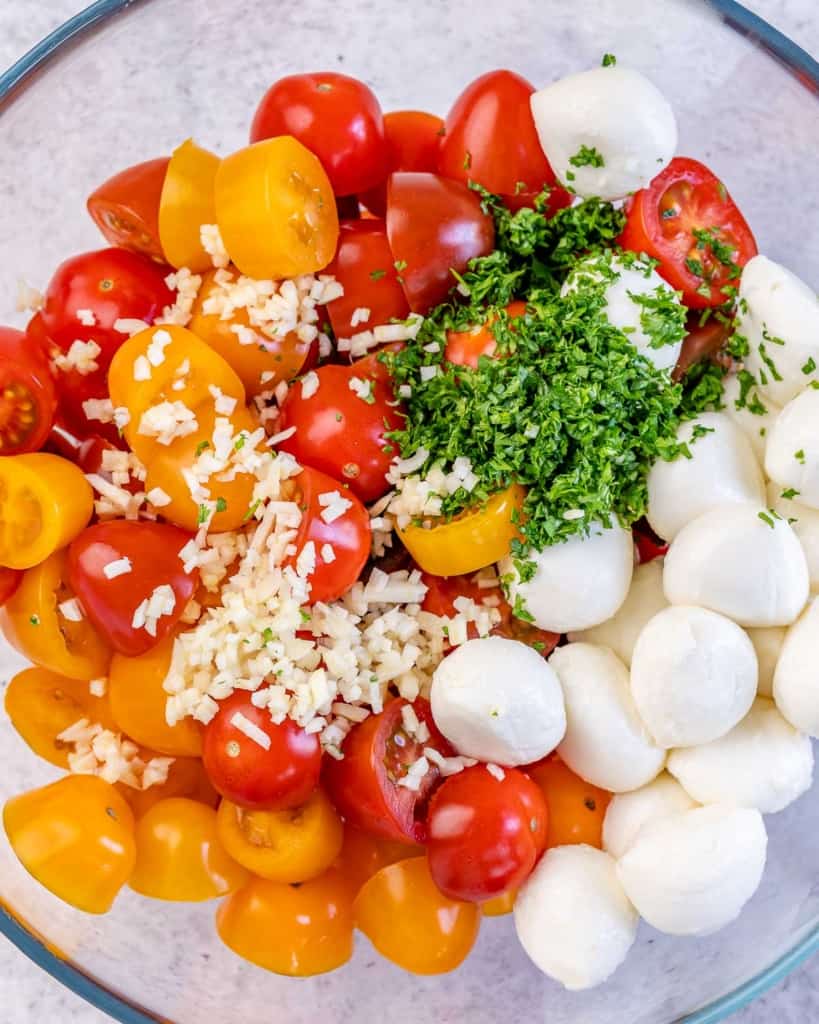 chopped tomatoes, cheese balls, and herbs in a bowl 
