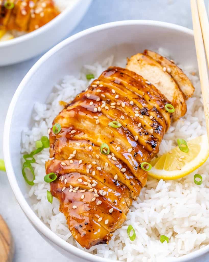 side shot of sliced baked teriyaki chicken over white rice 