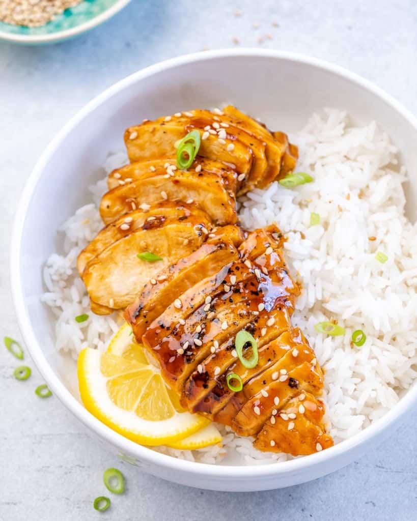 side shot of sliced teriyaki chicken over white rice and lemon garnish 