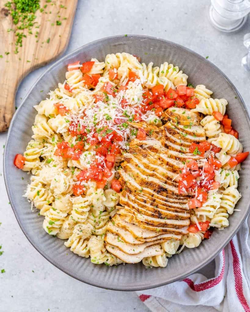 top view of chicken pasta in a gray bowl topped with freshly chopped tomatoes