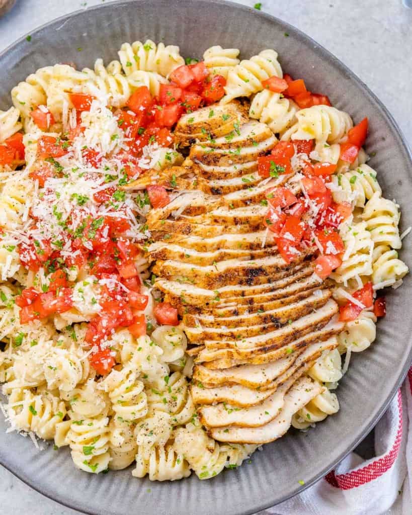 top view of pasta bowl with sliced cajun chicken breast, garnished with tomatoes and parmesan