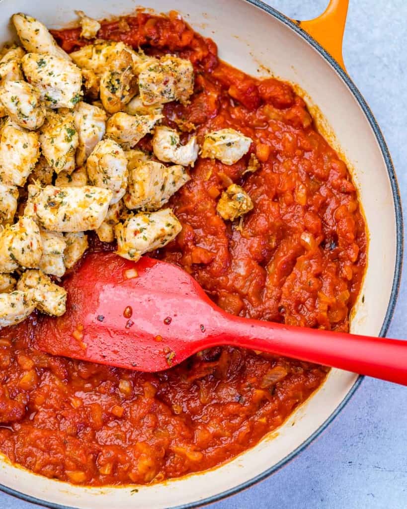 chicken bites over marinara sauce in a pan with a red spatula in it 