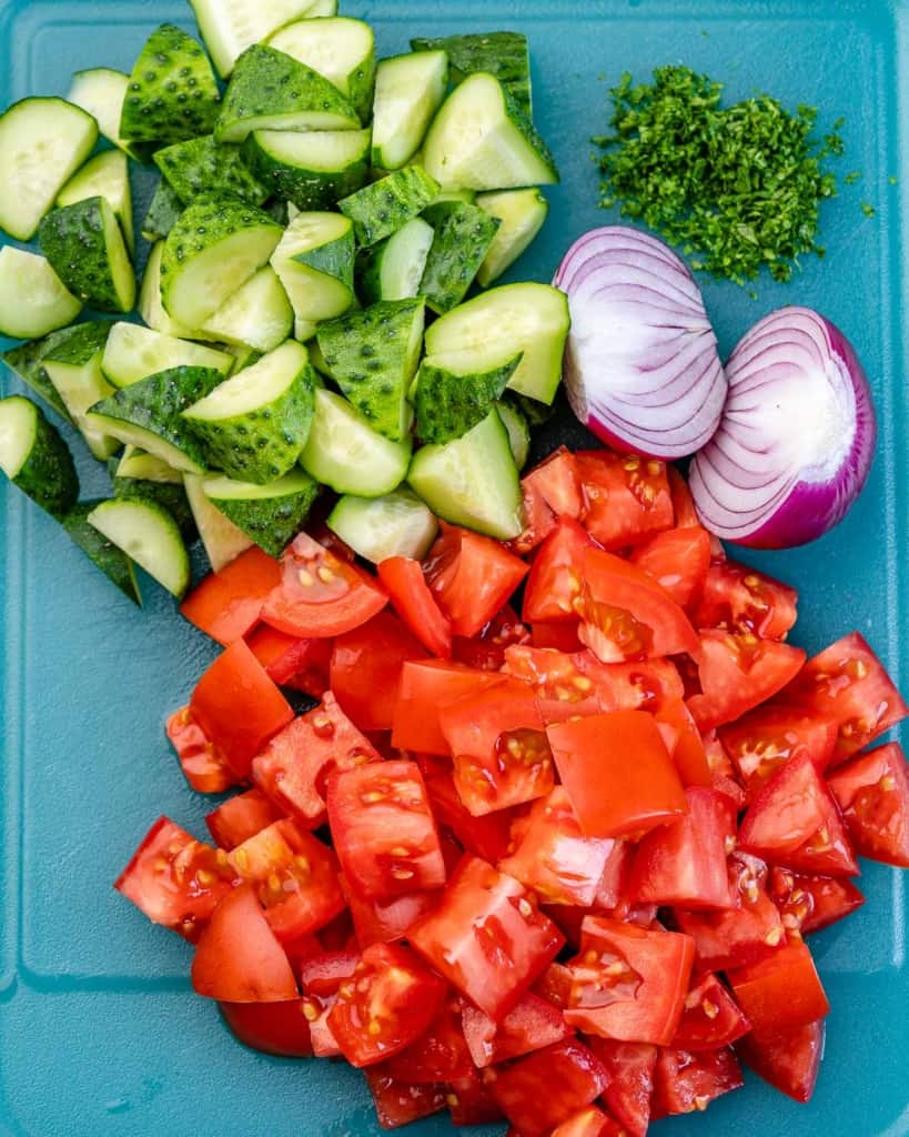 chopped tomatoes, onions, cucumbers, and parsley on a blue cutting board