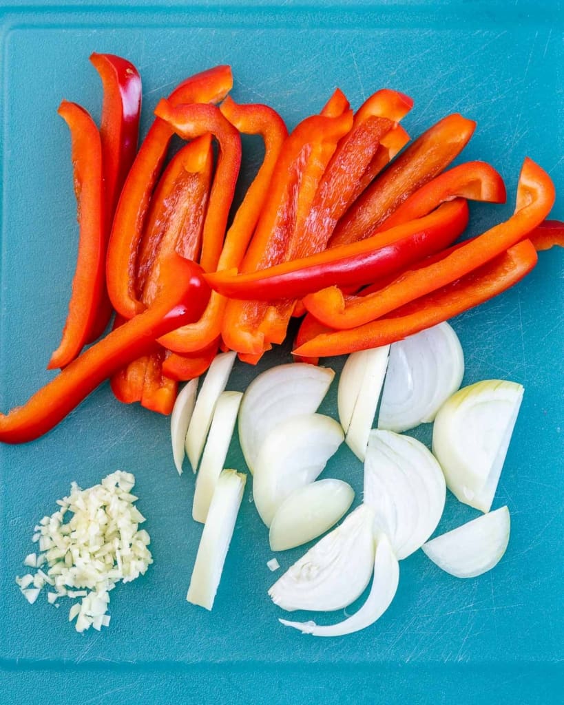 chopped bell pepper, onions, and garlic on a blue cutting board