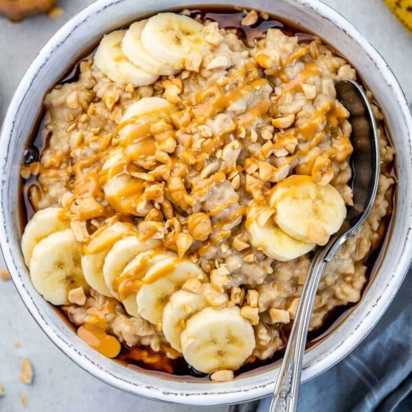 oatmeal bowl with sliced banana, peanut butter drizzle, and a spoon in bowl.