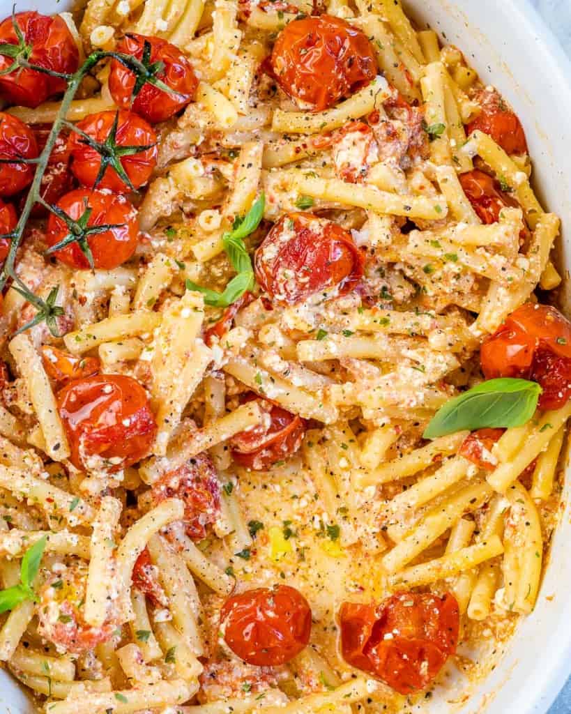 close up image of the baked feta pasta in a white dish with tomatoes 