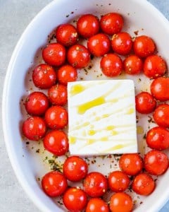 tomatoes around a block of feta cheese with olive oil drizzle