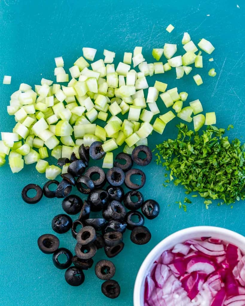 chopped olives, parsley, celery, and onions on a chopping board