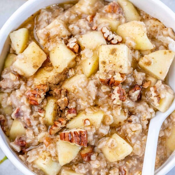 apple oatmeal bowl with a spoon in it topped with chopped pecans.