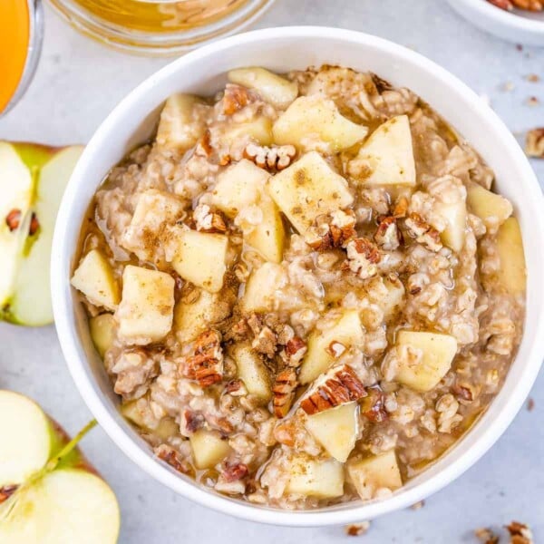 a white round bowl of chopped apples added over cooked oatmeal.