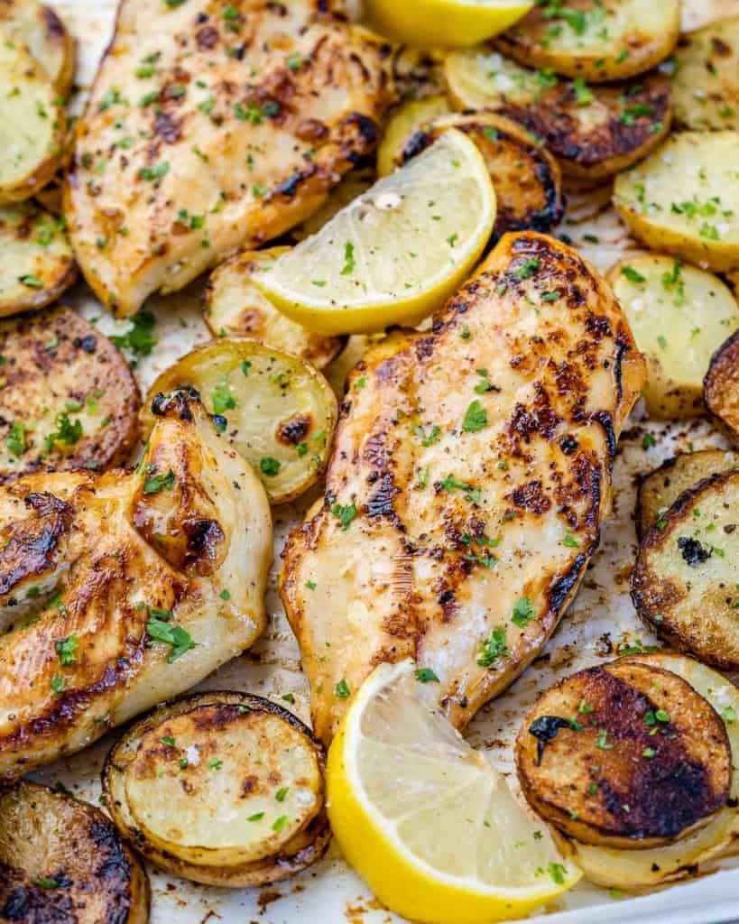 close up honey lemon chicken breast on a sheet pan with potatoes and lemon wedges 