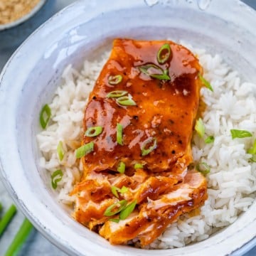 flaked baked honey salmon over white rice in a white bowl garnished with sliced green onions