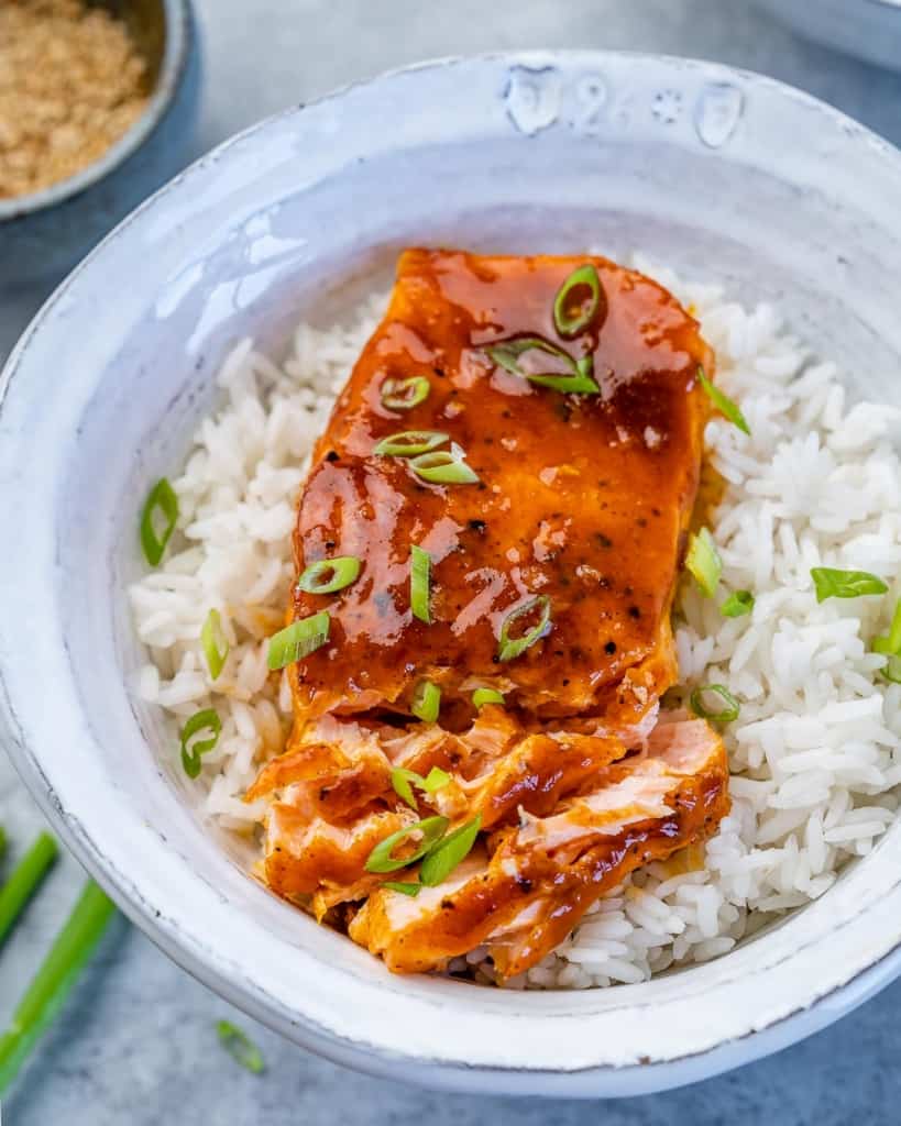 flaked baked honey salmon over white rice in a white bowl garnished with sliced green onions