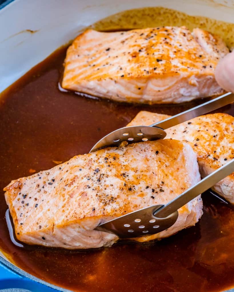 salmon filet being placed in honey glaze sauce 