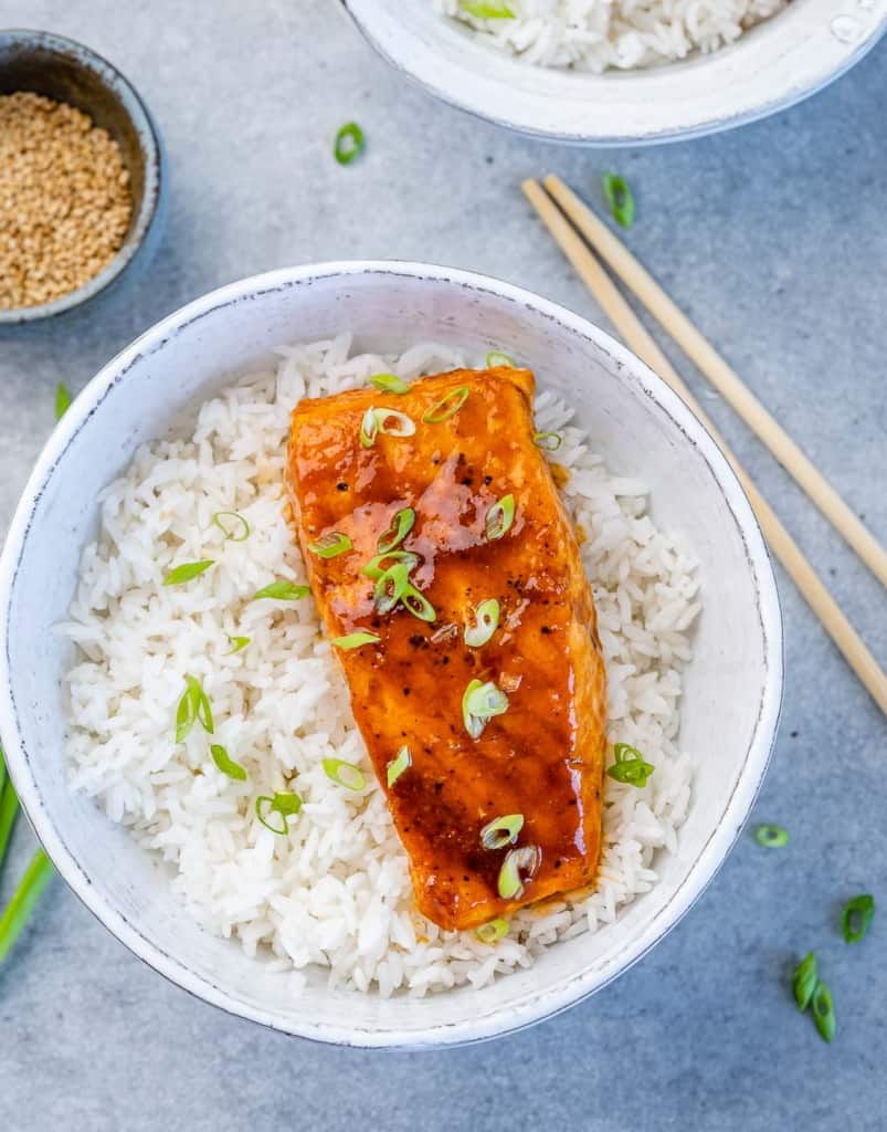 top view salmon filet over a bowl of rice garnished with green onions with chop sticks on the side