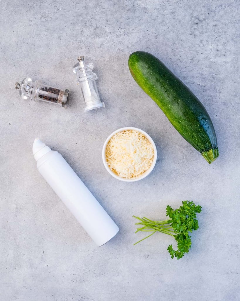zucchini, parmesan, salt and pepper, cooking spray, and parsley on a flat surface 