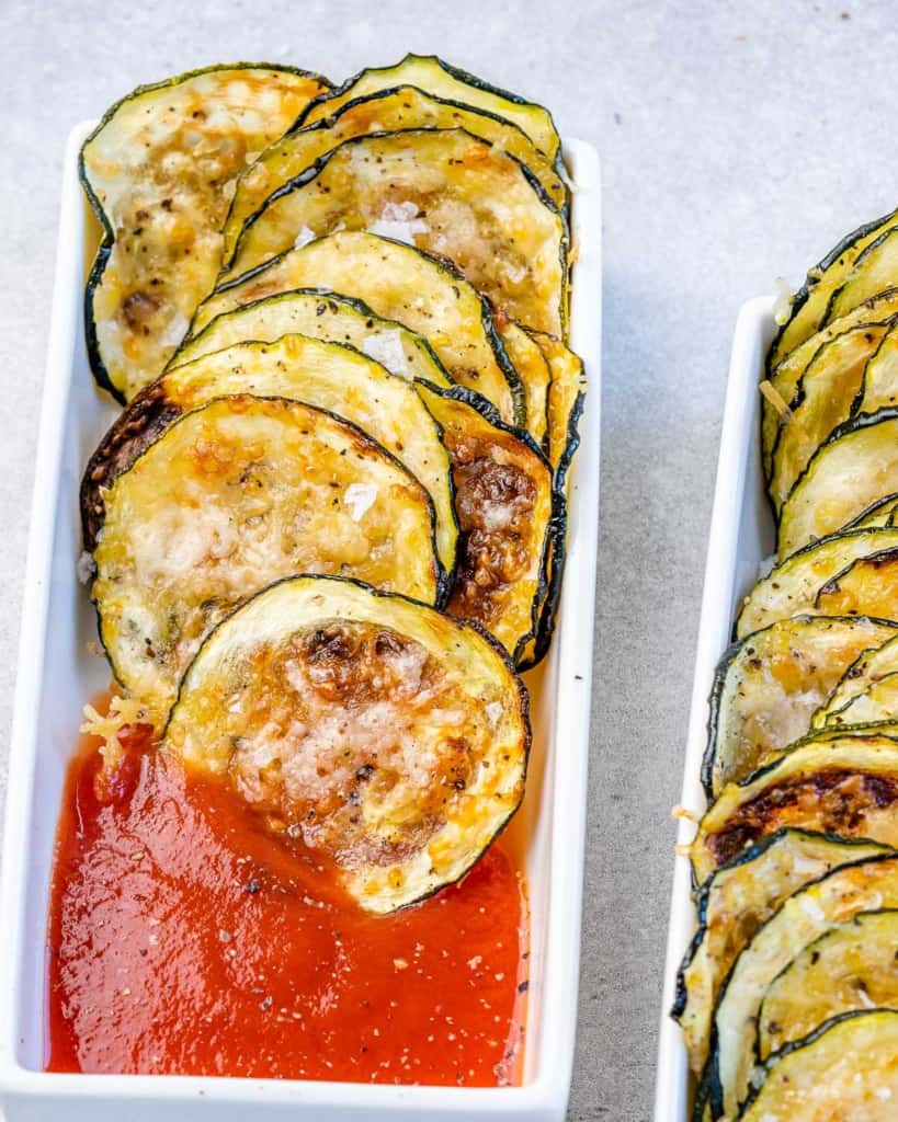 close up image of zucchini chips next to marinara in a white dish