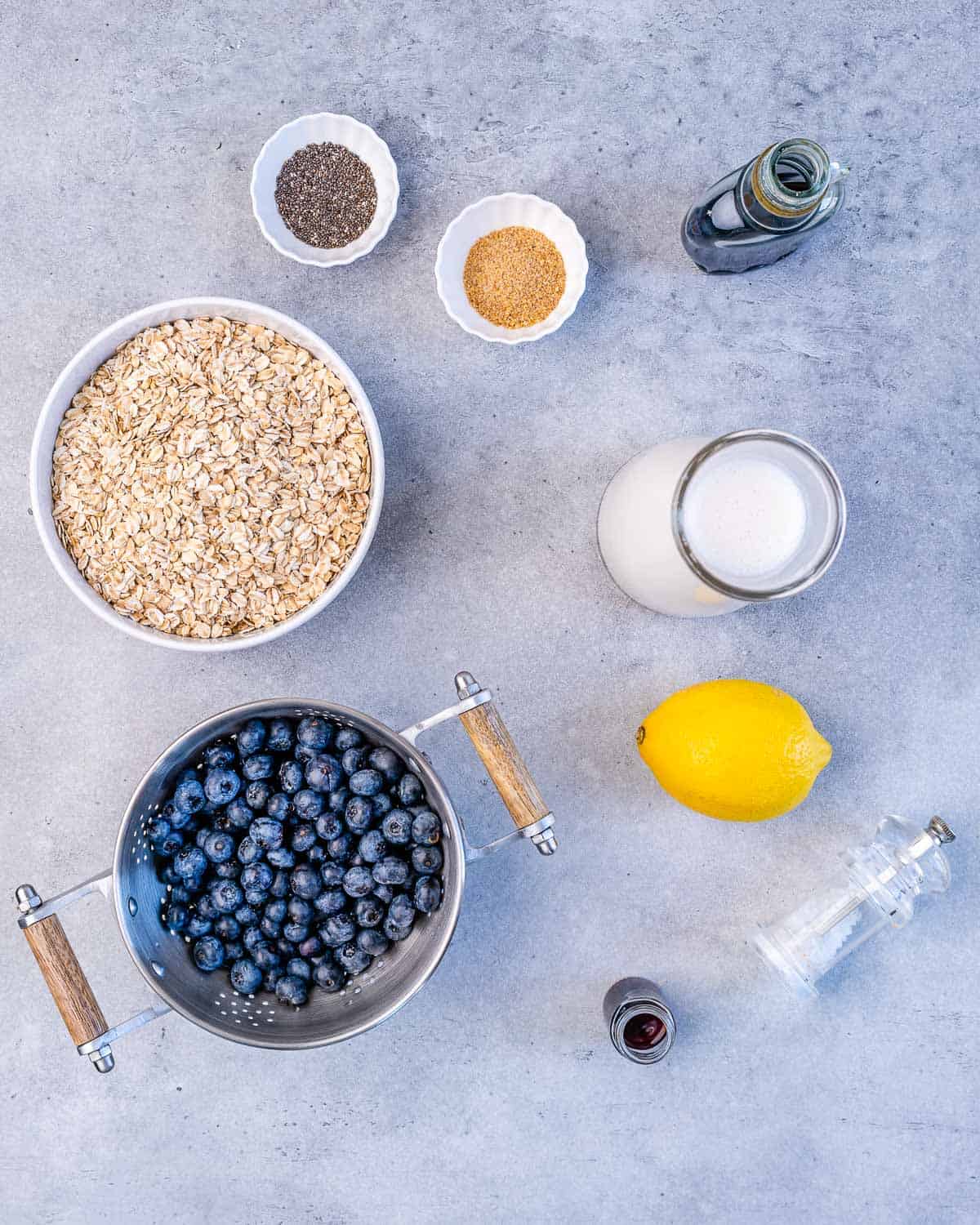 chia seeds, flax seeds, oats, lemon, milk, maple syrup, blueberries, salt, vanilla on grey surface