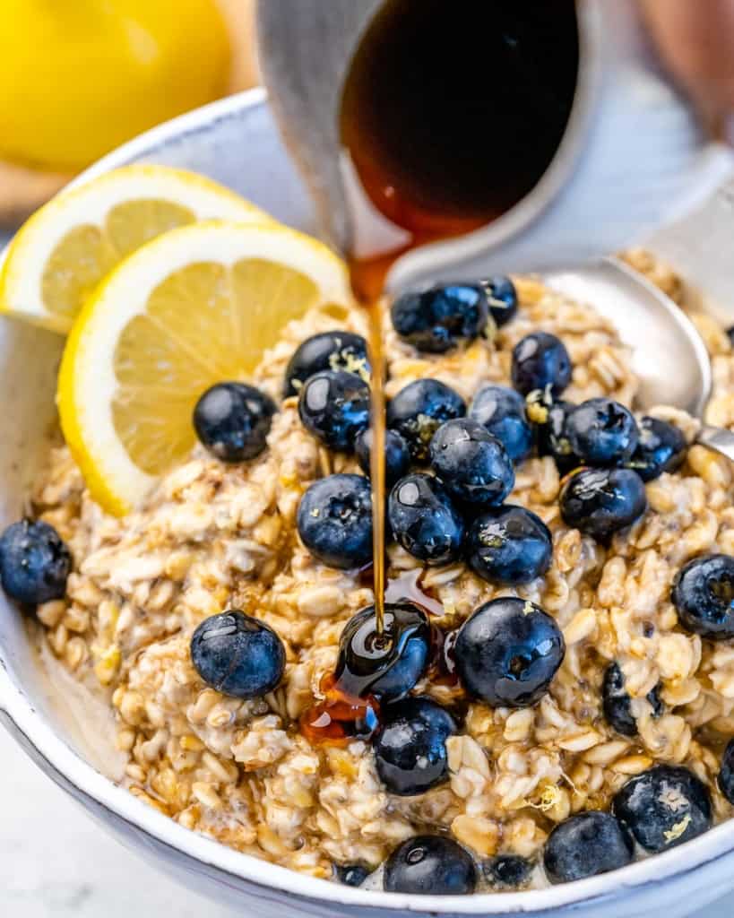 maple syrup being poured over overnight oatmeal with blueberries