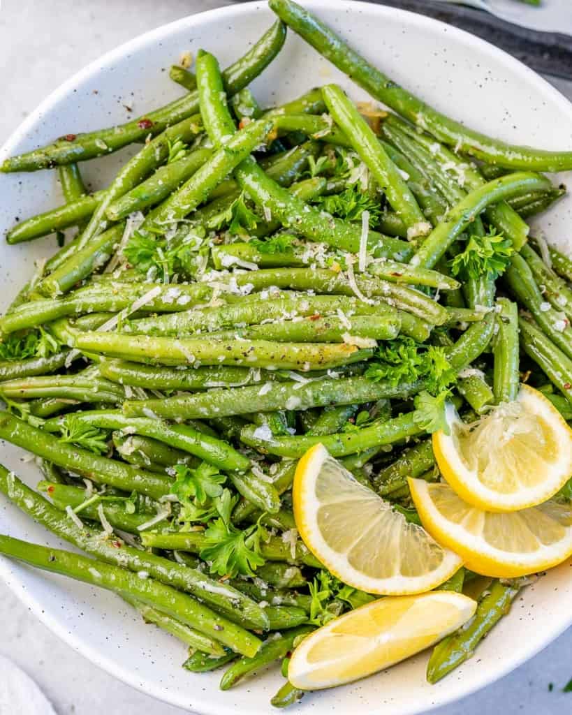 top view close up image of roasted green beans on a plate with lemon garnishes 
