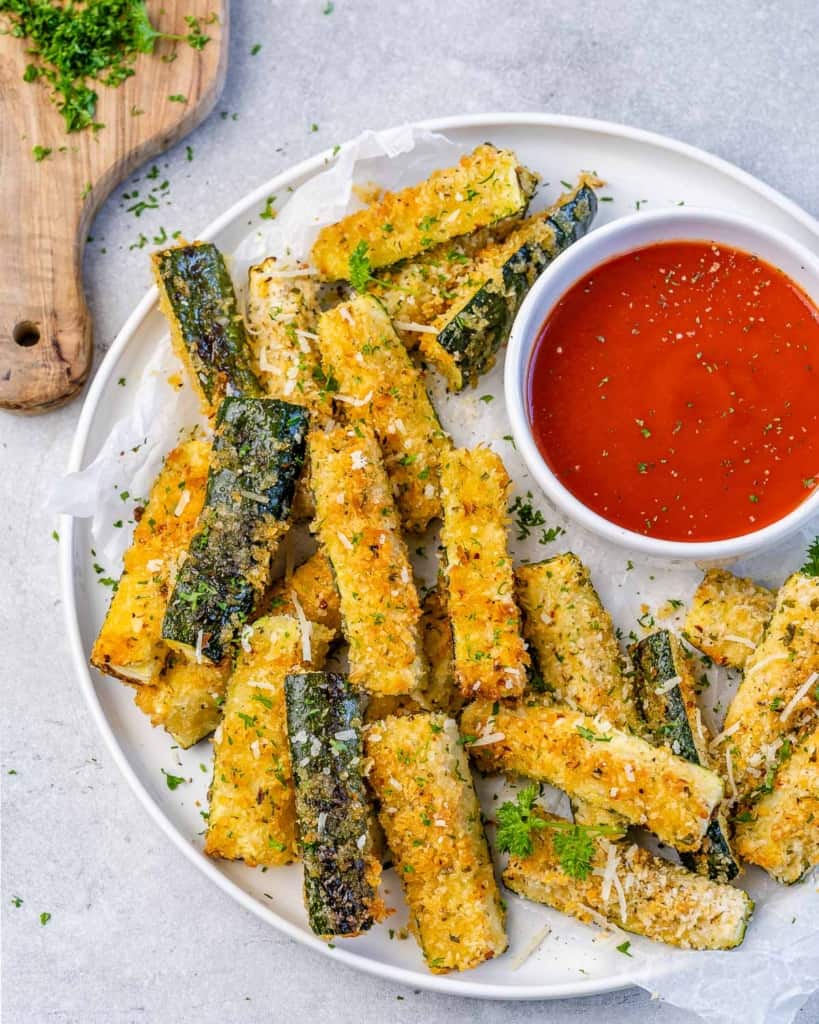 top view of zucchini fries on a white plate with red sauce on the side 
