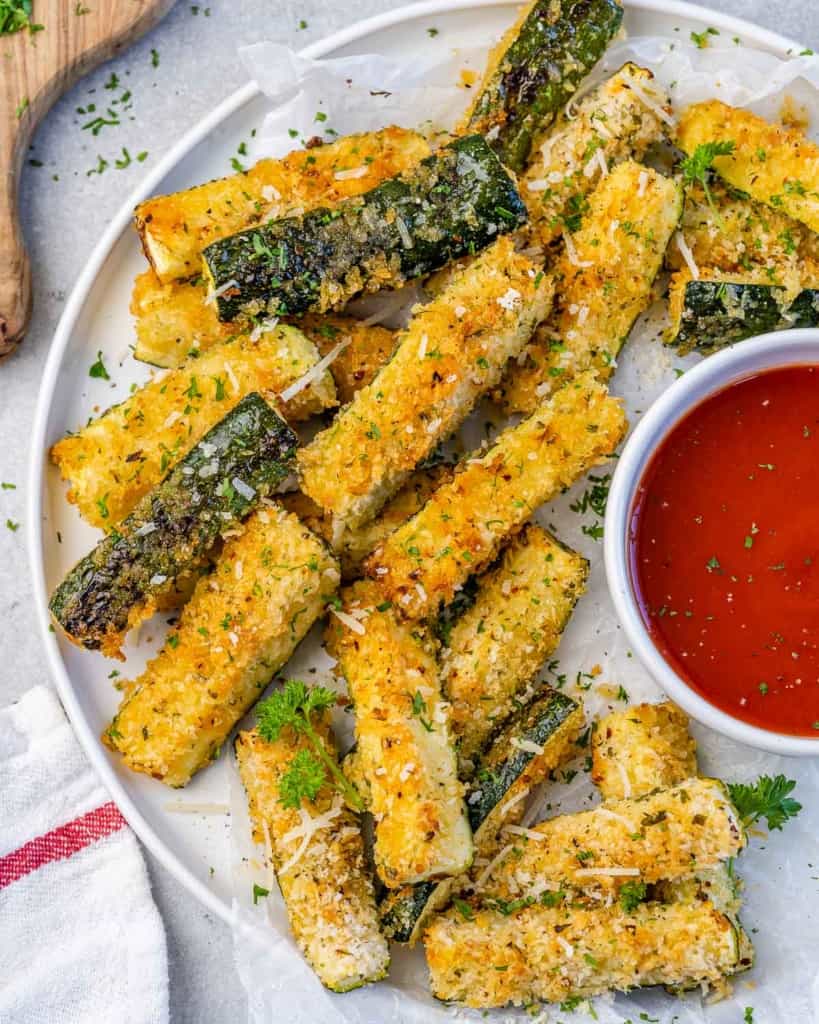 close up zucchini fries with a side of red dipping sauce on a white plate 