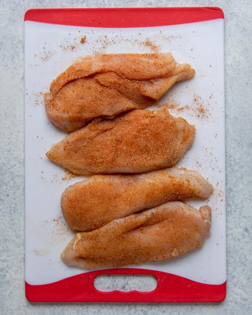 seasoned raw chicken breast on a white and red cutting board