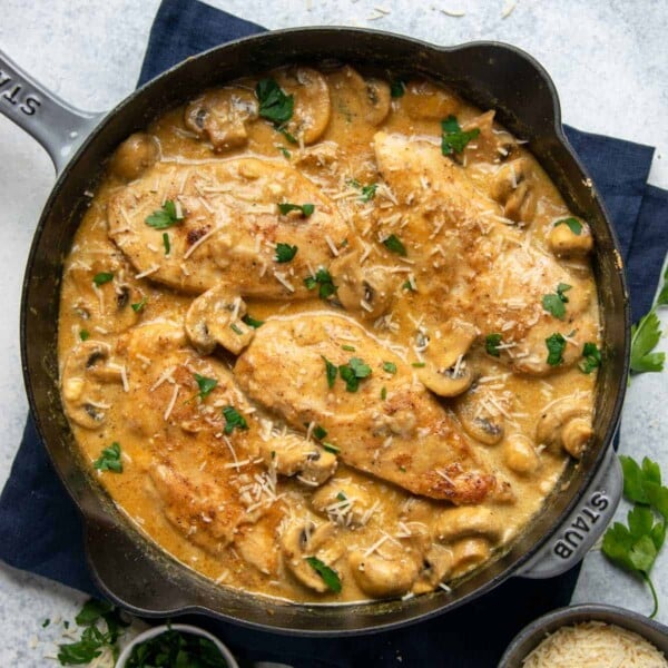 top view chicken breasts in a creamy mustard and mushroom sauce in a black skillet