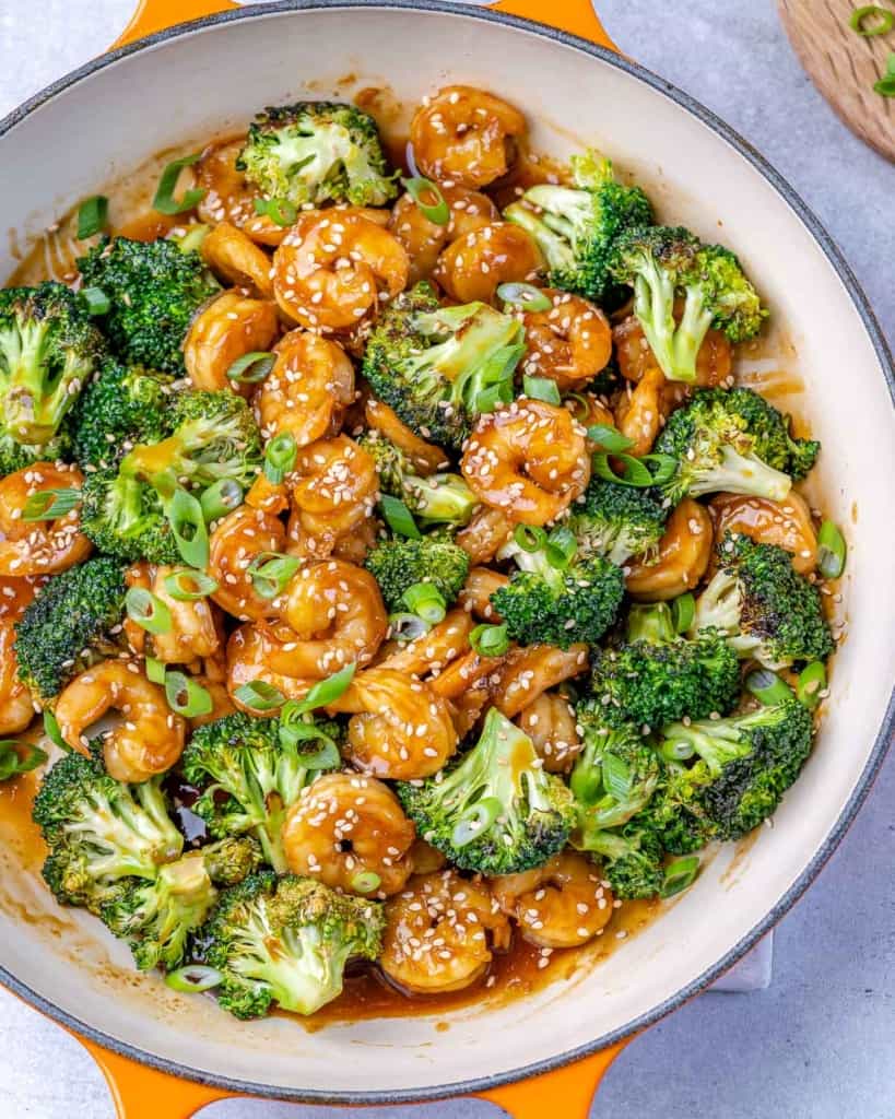cooked shrimp and broccoli in orange skillet with sesame seeds