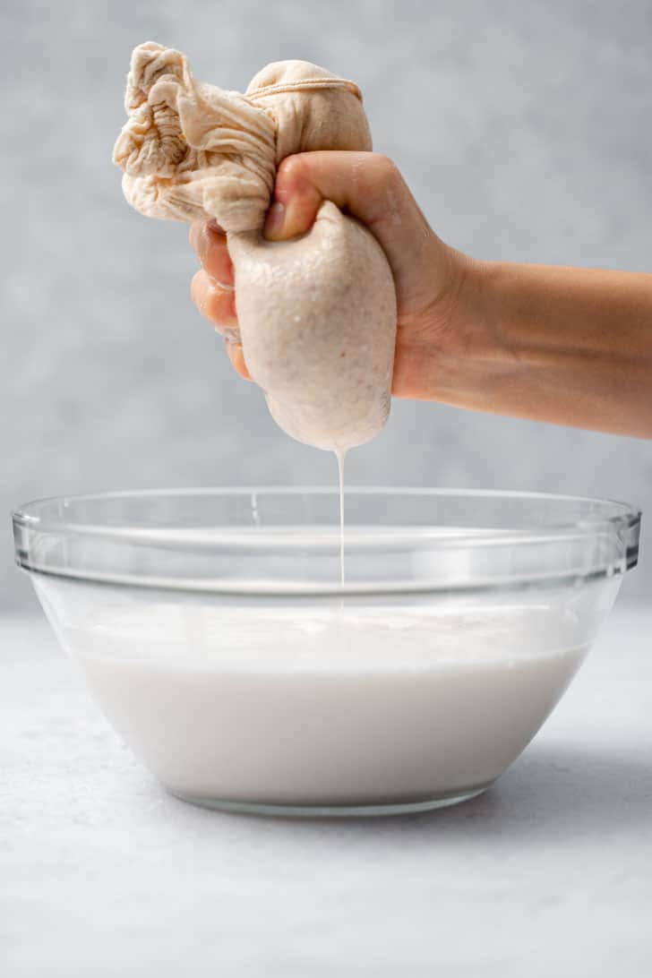 squeezing almond milk with nut milk bag over bowl