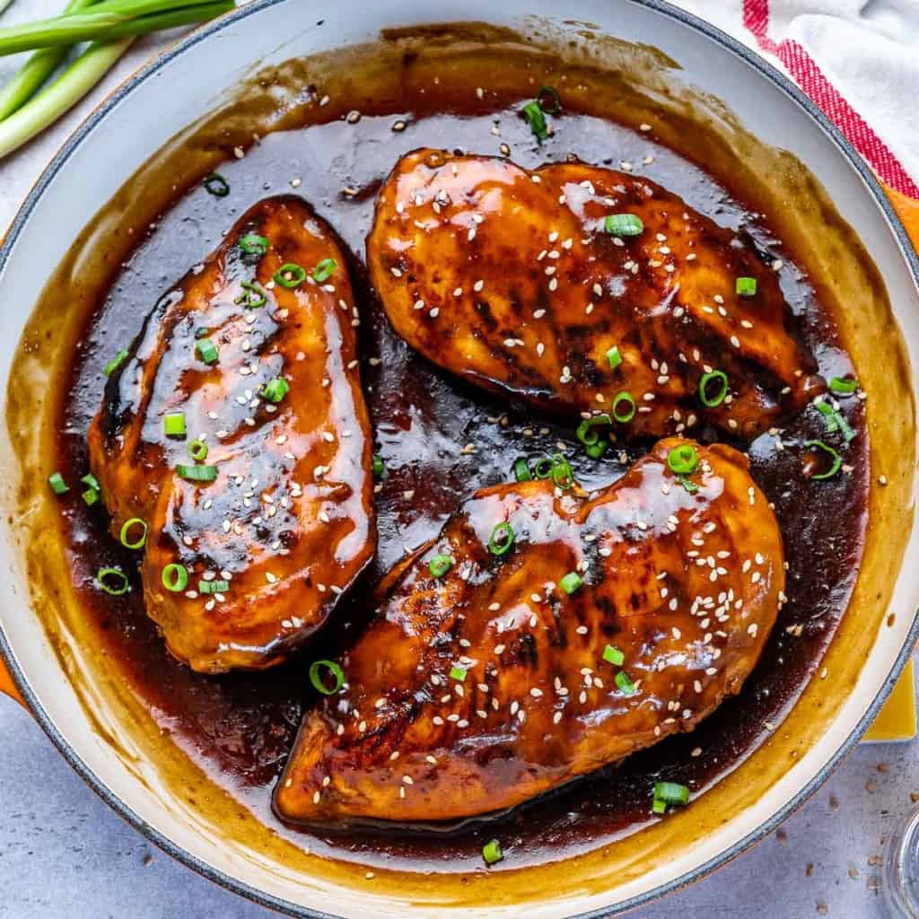 top view of 3 chicken breasts with asian chili glaze in a yellow skillet