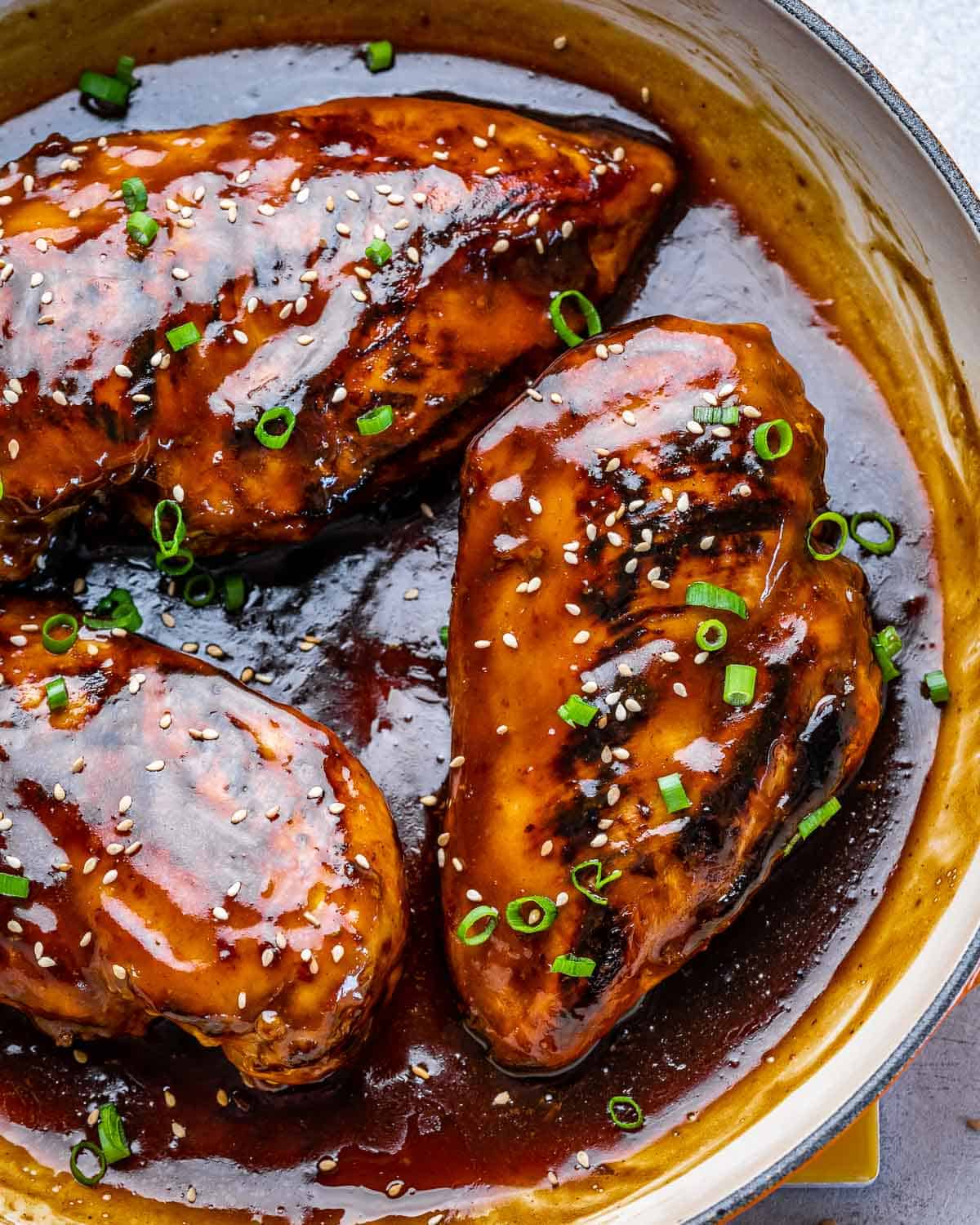 top view of Asian chili chicken breasts in pan with sauce and sesame seeds 