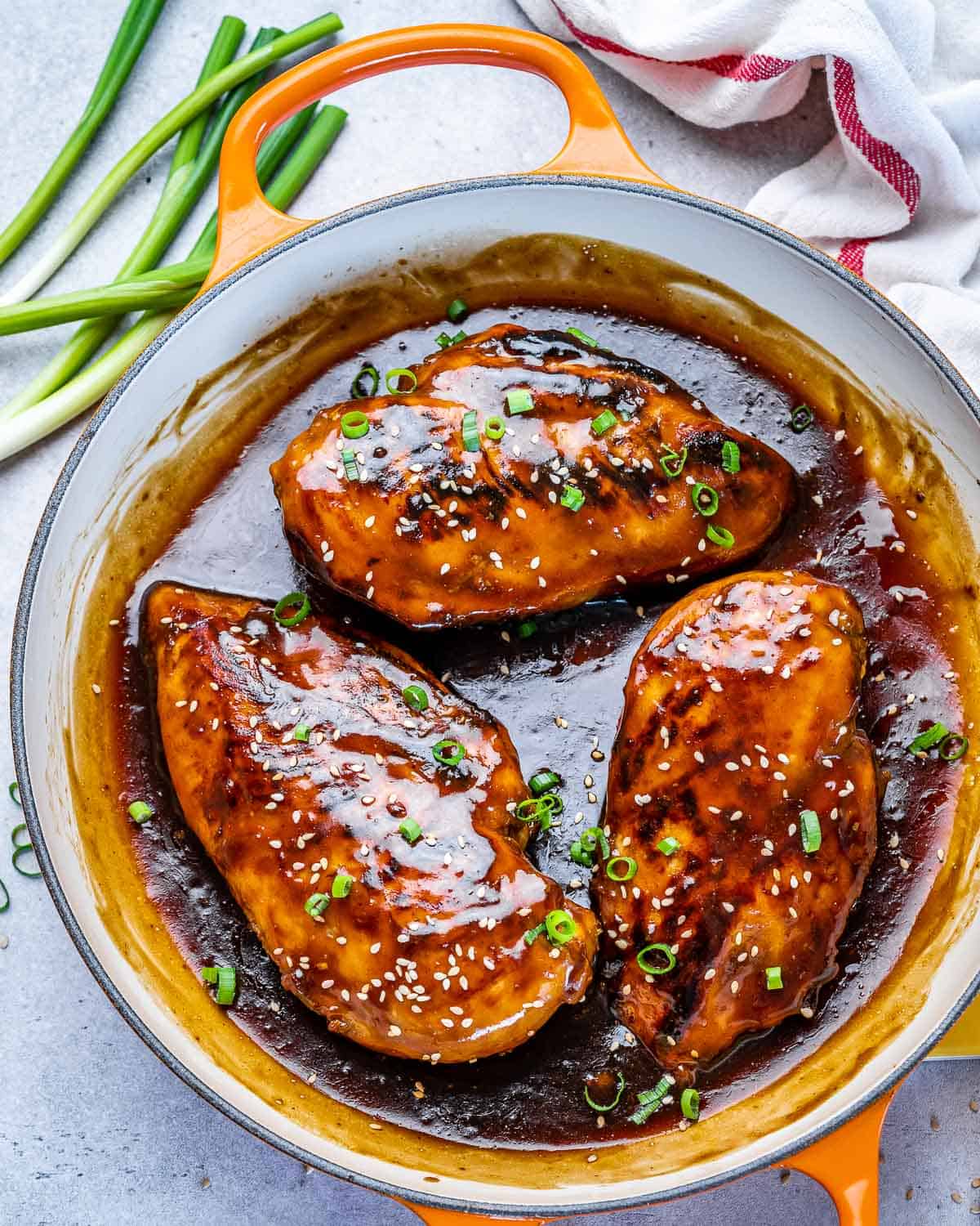 top view of four chicken breasts in sauce with green onions and sesame seeds