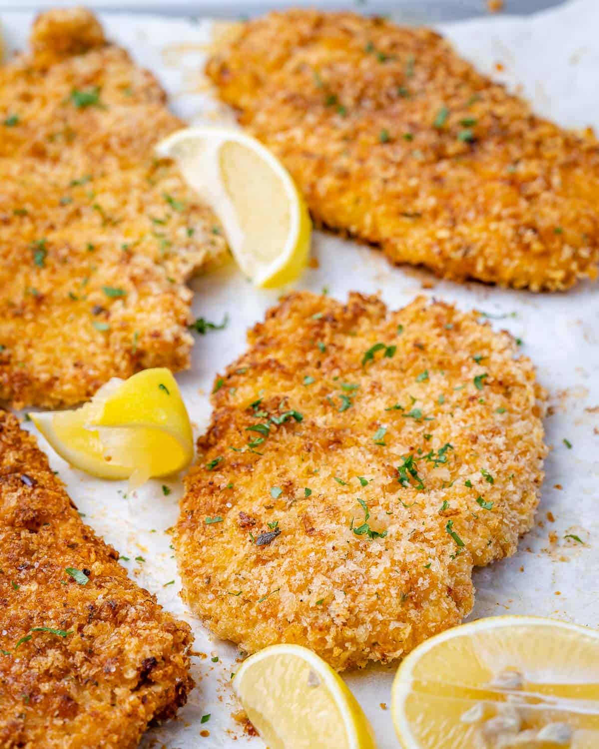 close view of chicken coated in parmesan breadcrumbs with lemon wedges