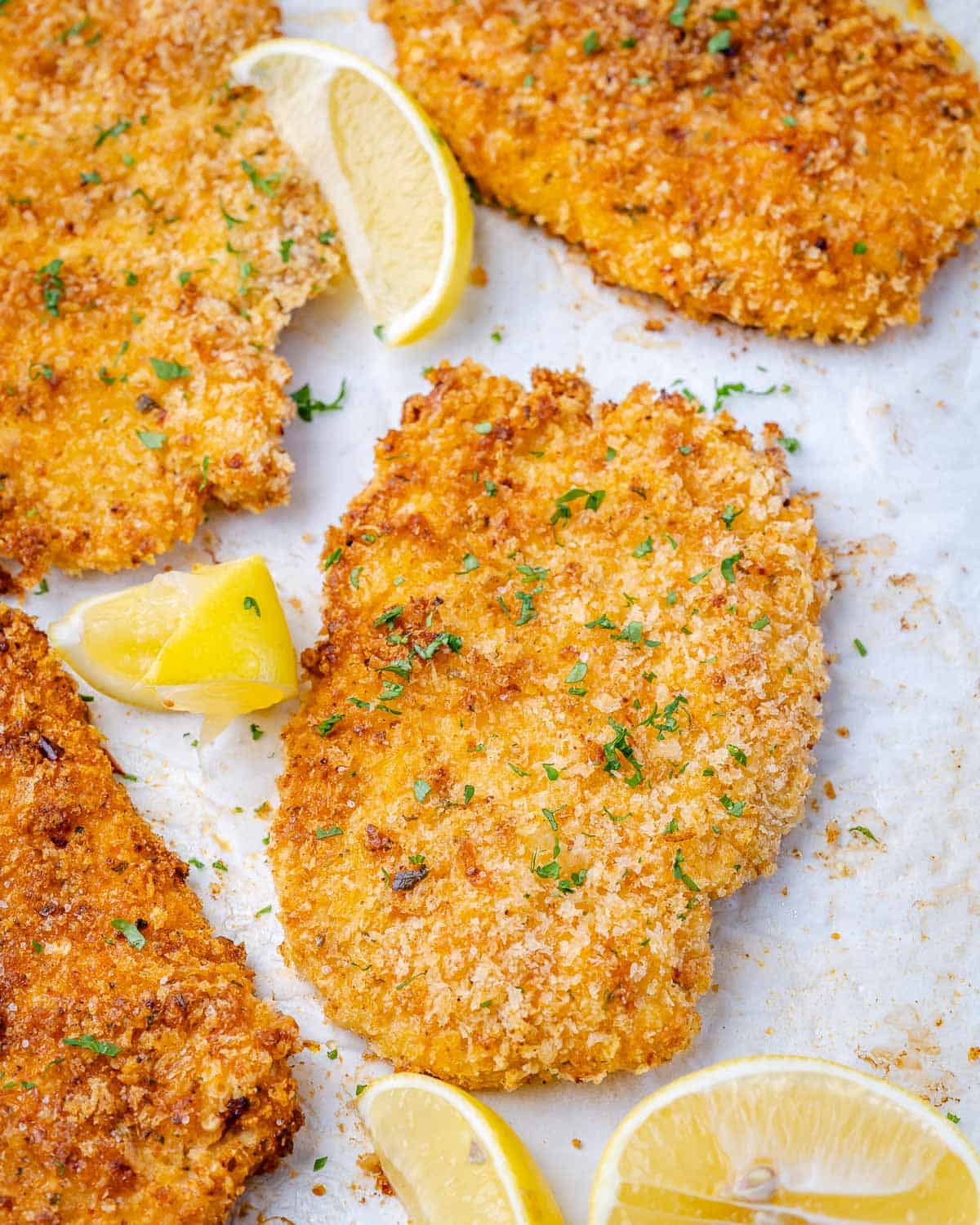 close view of parmesan baked chicken with lemon wedges and breadcrumbs