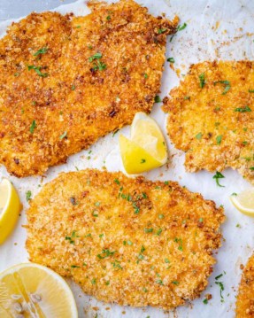 top view of crispy chicken cutlets with lemon wedges and parsley garnishes