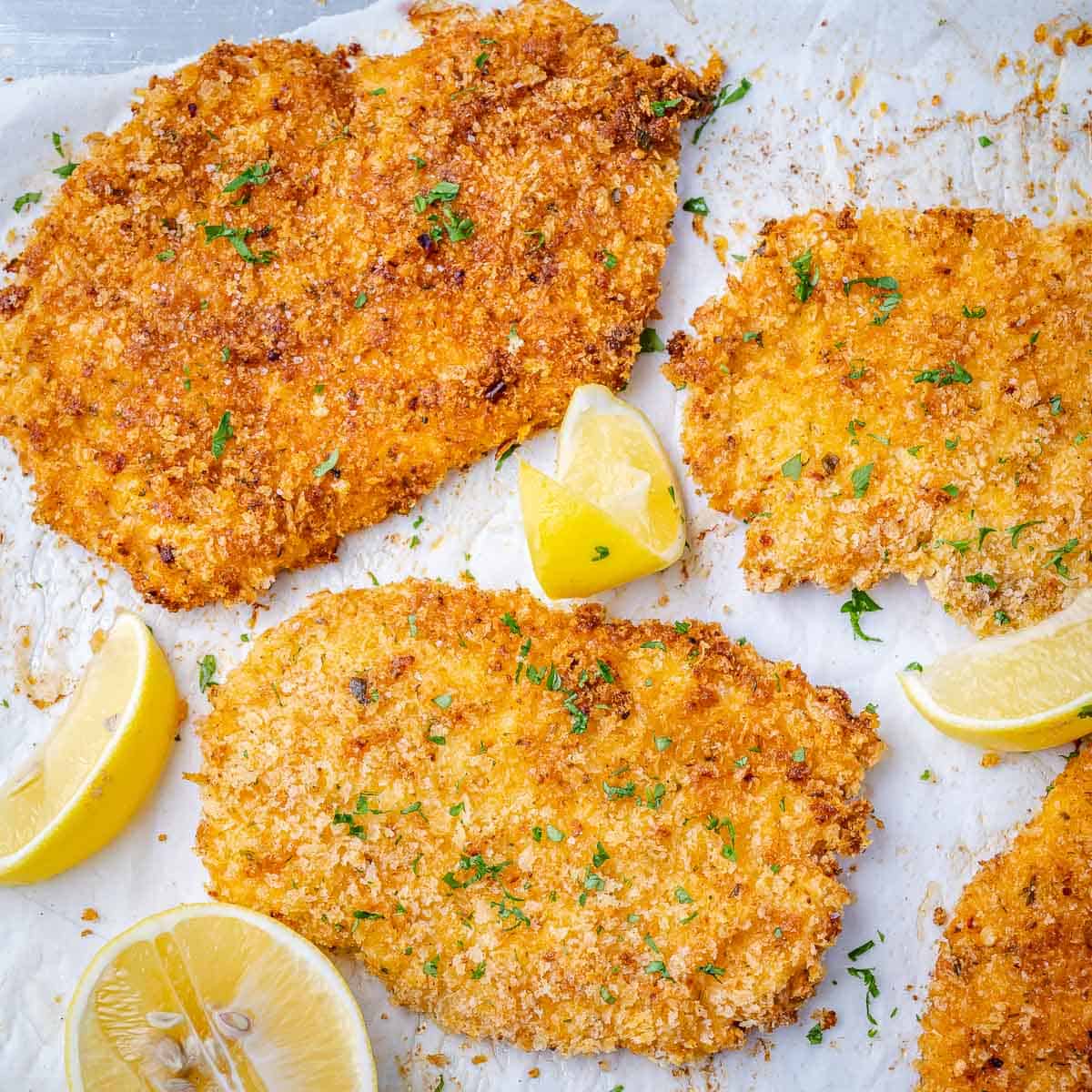 top view of crispy chicken cutlets with lemon wedges and parsley garnishes