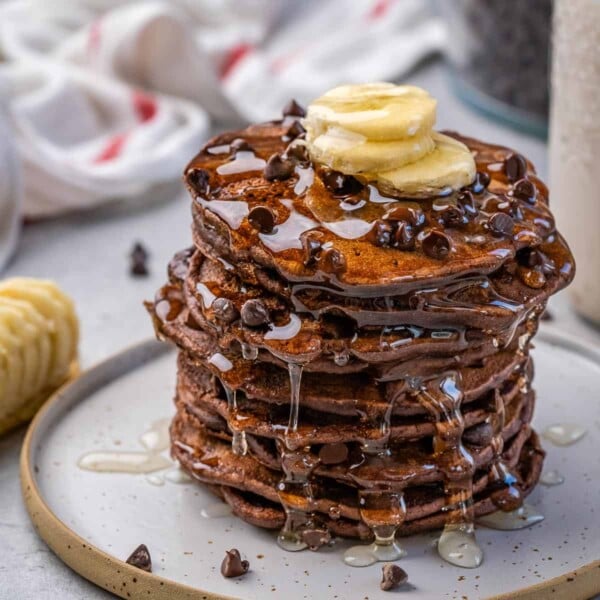 side shot of stacks of chocolate pancakes topped with bananas syrup and chocolate chips