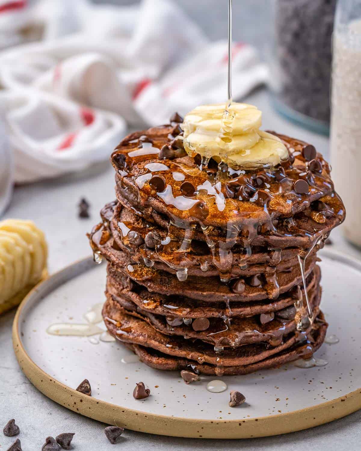 stack of chocolate pancakes with banana, chocolate chips, syrup