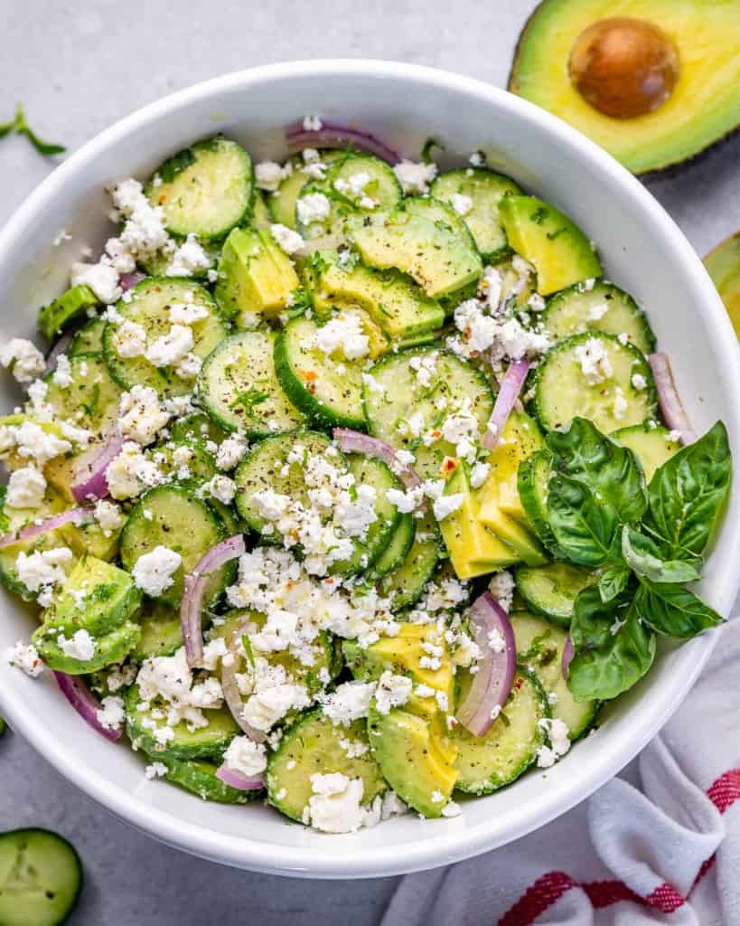 top view of cucumber salad in a white bowl with feta and avocado 