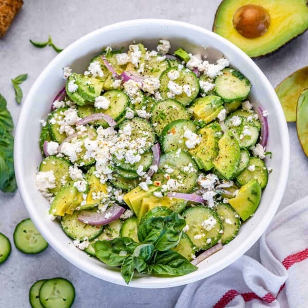 a white round bowl with cucumber avocado and feta salad with basil garnish.