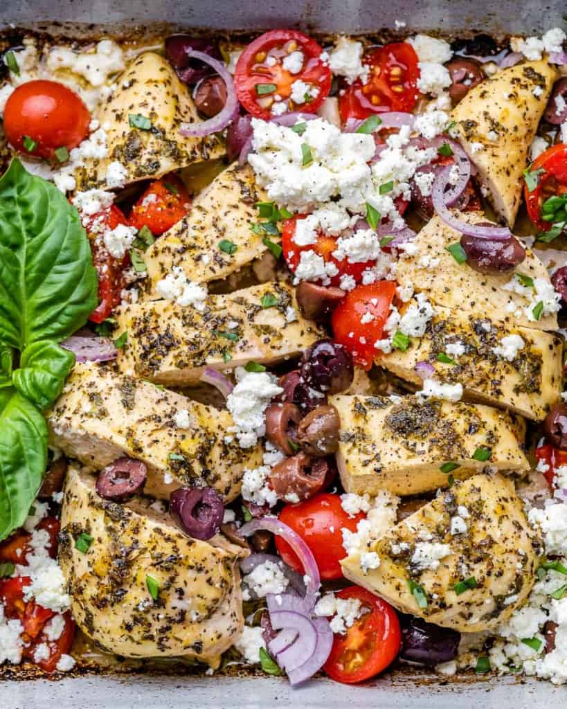 tope view sliced chicken breast baked in a white dish with tomatoes olives and feta cheese