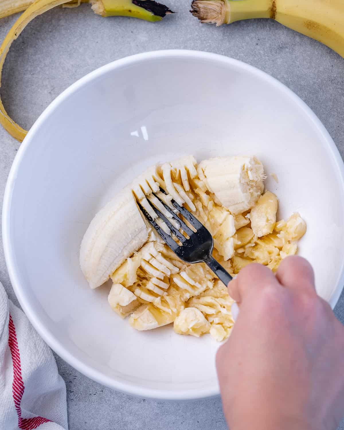 mashing banana in white bowl with fork